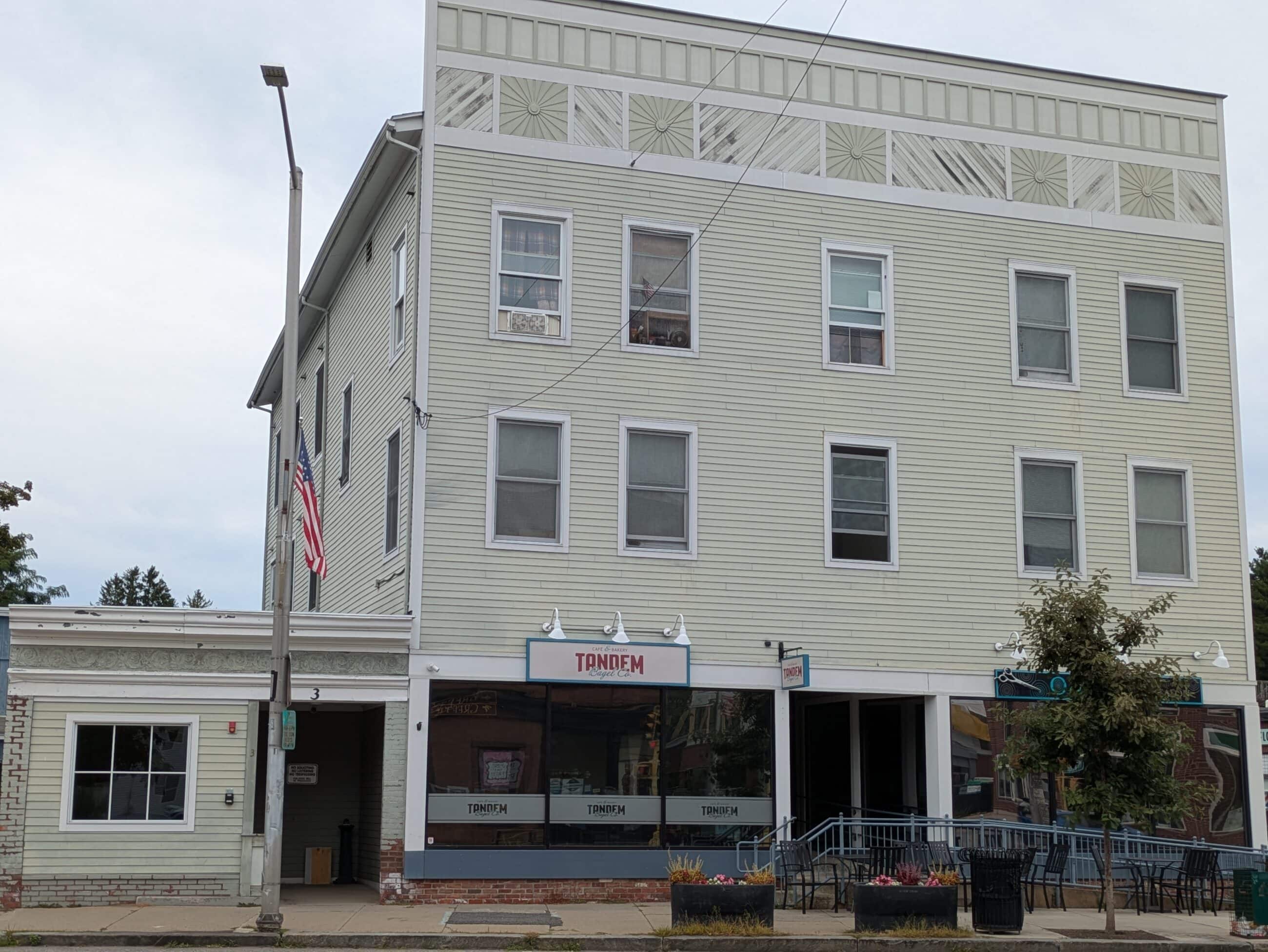 Old Maine Block building. The building is off-white with white shutters. Stores "TANDEM" and "ON POINT" can be seen in view.