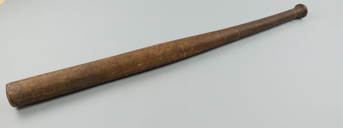 Photo of a wooded baseball bat, with a textured grip made out of turned wood at the base. Grey background.