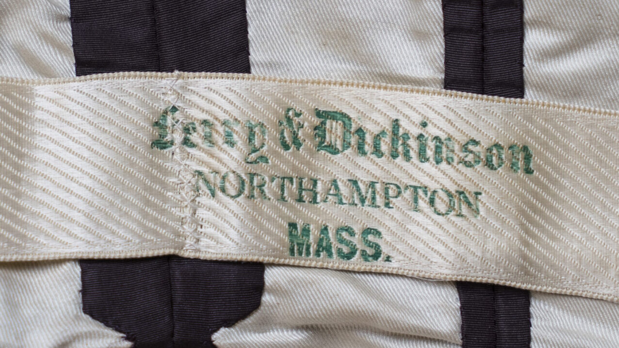 Photograph of a tag attached to a piece of clothing. The tag is yellowed white with green lettering.