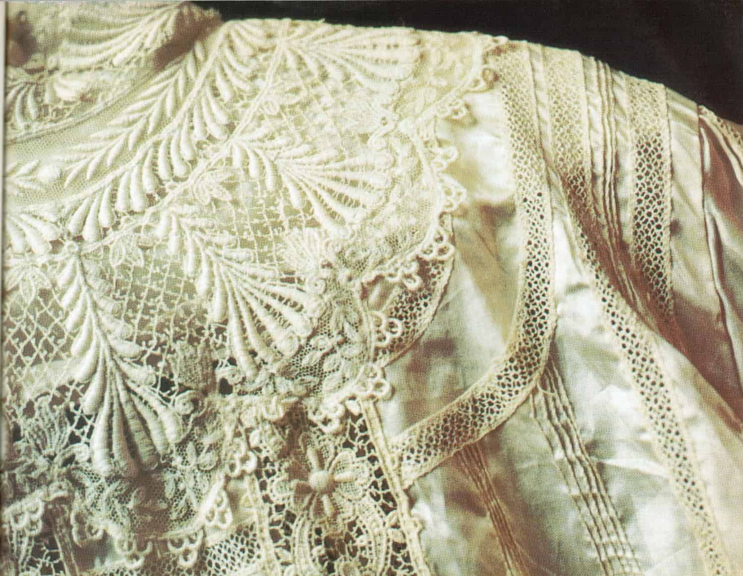 Photograph of the shoulder of a dress. The dress is a yellowed white with floral lace designs. 