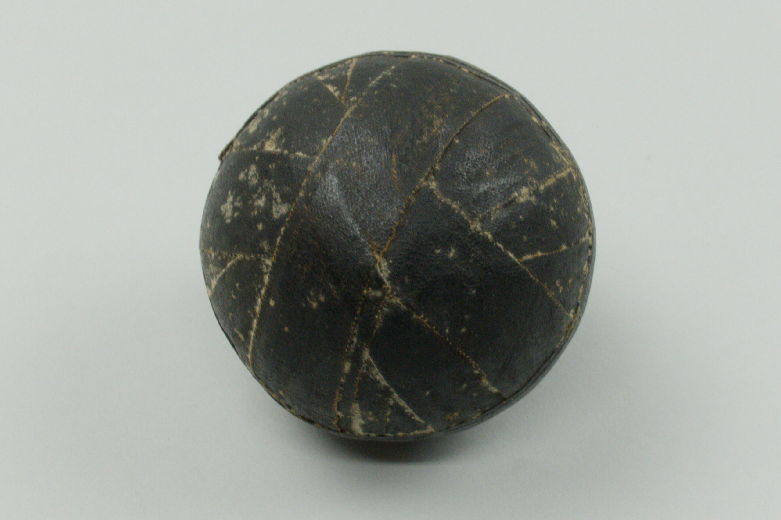 Photograph of an old, small ball, completely covered in layers of black electrical tape wrapped around it. Grey background. 