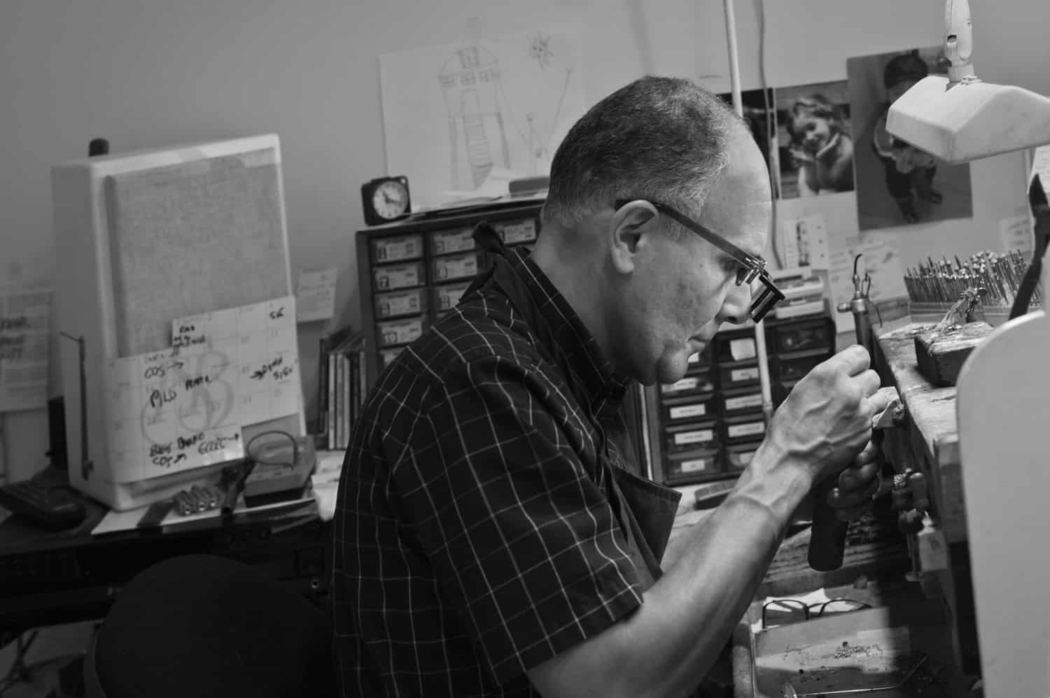 Black-and-white photograph of a matured man sitting at his desk working on something. He is faced away from the camera.