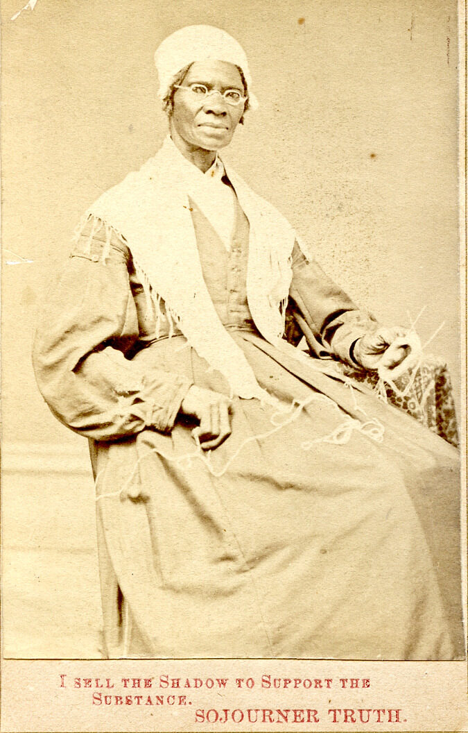 Black-and-white photographic portrait of Sojourner Truth sitting in a chair. She has yarn on her lap and knitting tools. She wears a dark dress with a white material draped on her shoulders and she has a white bonnet or cap on her head. Framing the image is yellowed paper. Below the image it has been printed in red: "I SELL THE SHADOW TO SUPPORT THE SUBSTANCE. SOJOURNER TRUTH."