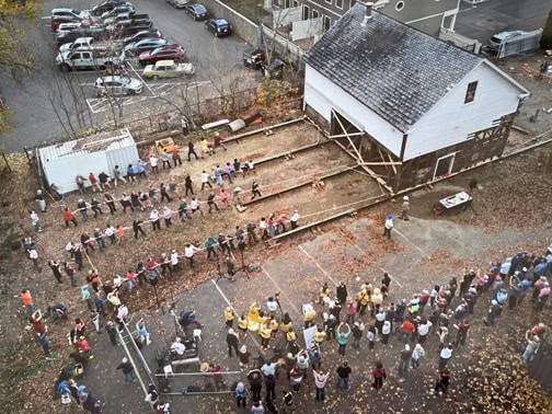 Arial view of scores of people helping to raise a barn.