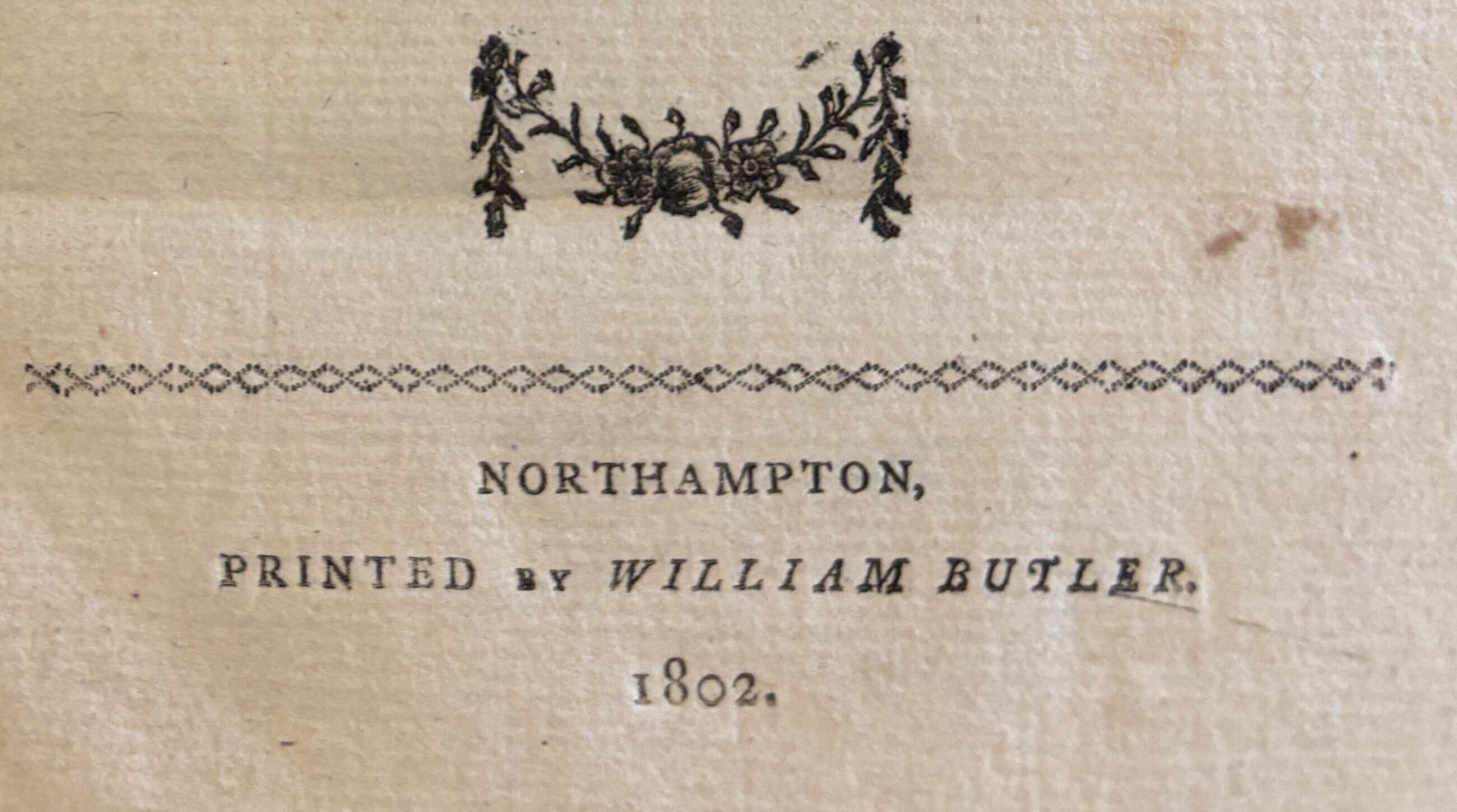 A section of the front page of book. A small floral design shaped like an 'M' is over a chain-like design dividing the design from the bottom text. Below reads, in print: "NORTHAMPTON, PRINTED BY WILLIAM BUTLER. 1802."