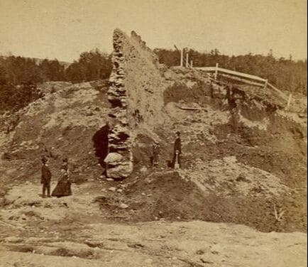 old photograph of remains of reservoir dam and people standing at the foot of the dry reservoir bed