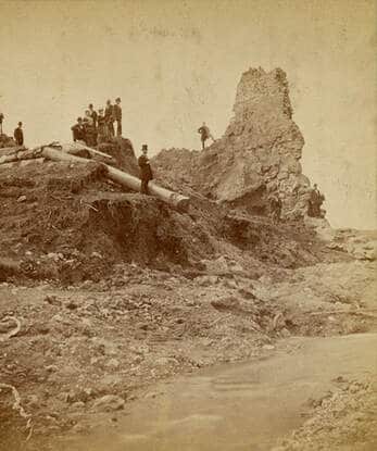 old photograph of remains of a group of people standing on a hill with remains of the reservoir dam in background