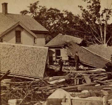 Bits of buildings and roofs scattered about in a chaotic scene, with a couple of men looking at the rubble.