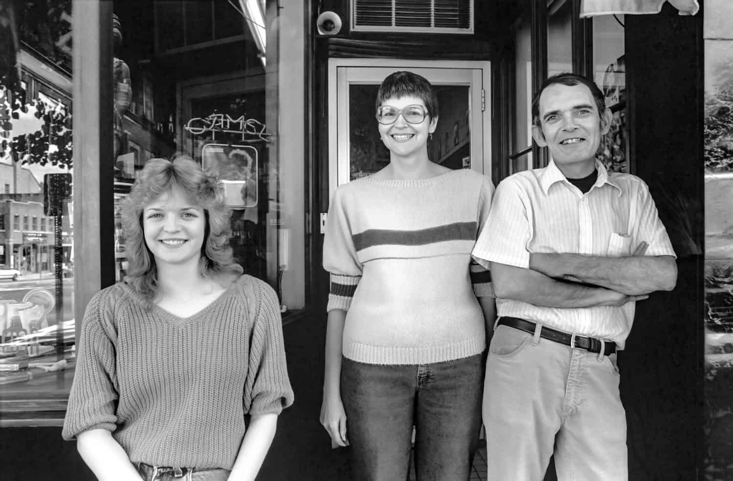 Left to right: Maureen, Flo, and Bill Collins. Black-and-white photograph. Bill and Flo stand next to their young adult daughter Maureen in front of smoke shop. 