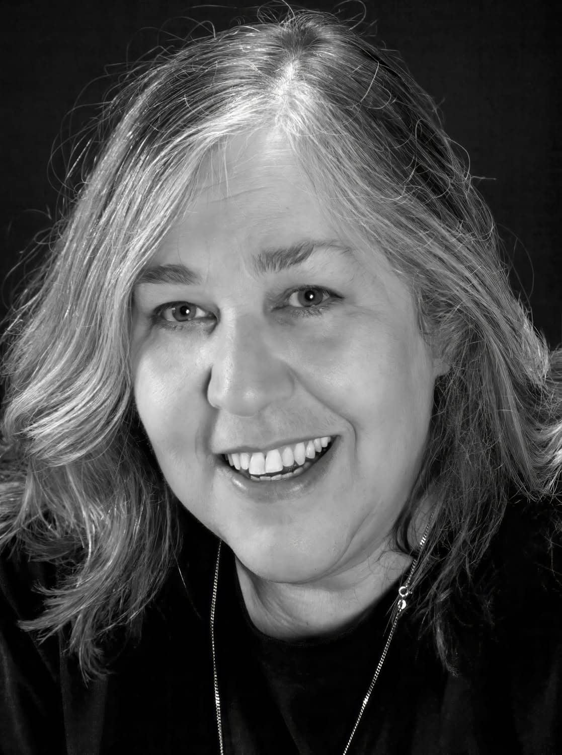 Black-and-white photographic portrait of a middle aged woman with dark graying hair. She smiles at the camera.