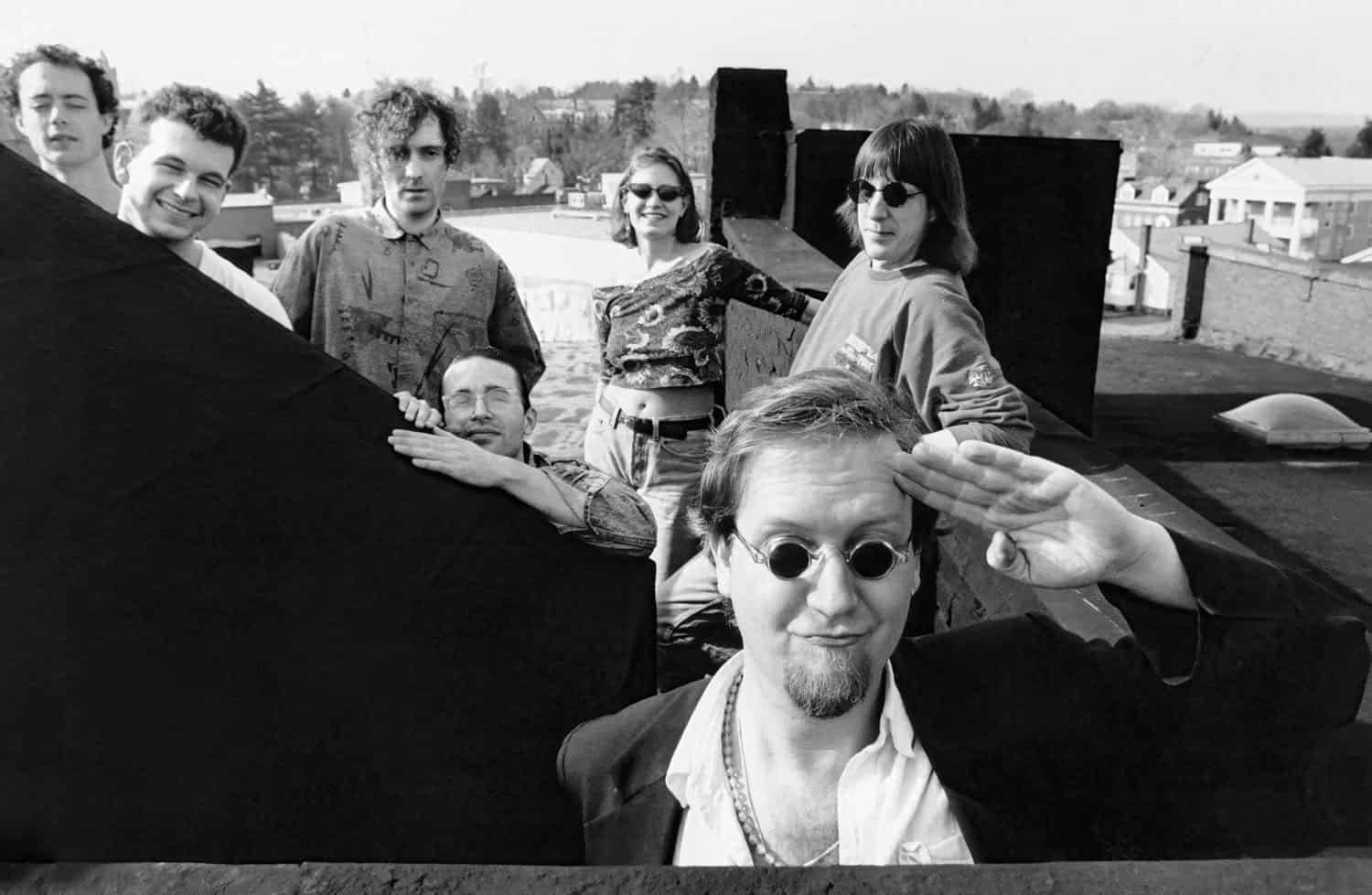 Black-and-white photograph of a group of young musicians. There are seven of them and they appear on a roof. There are 6 men and one woman.
