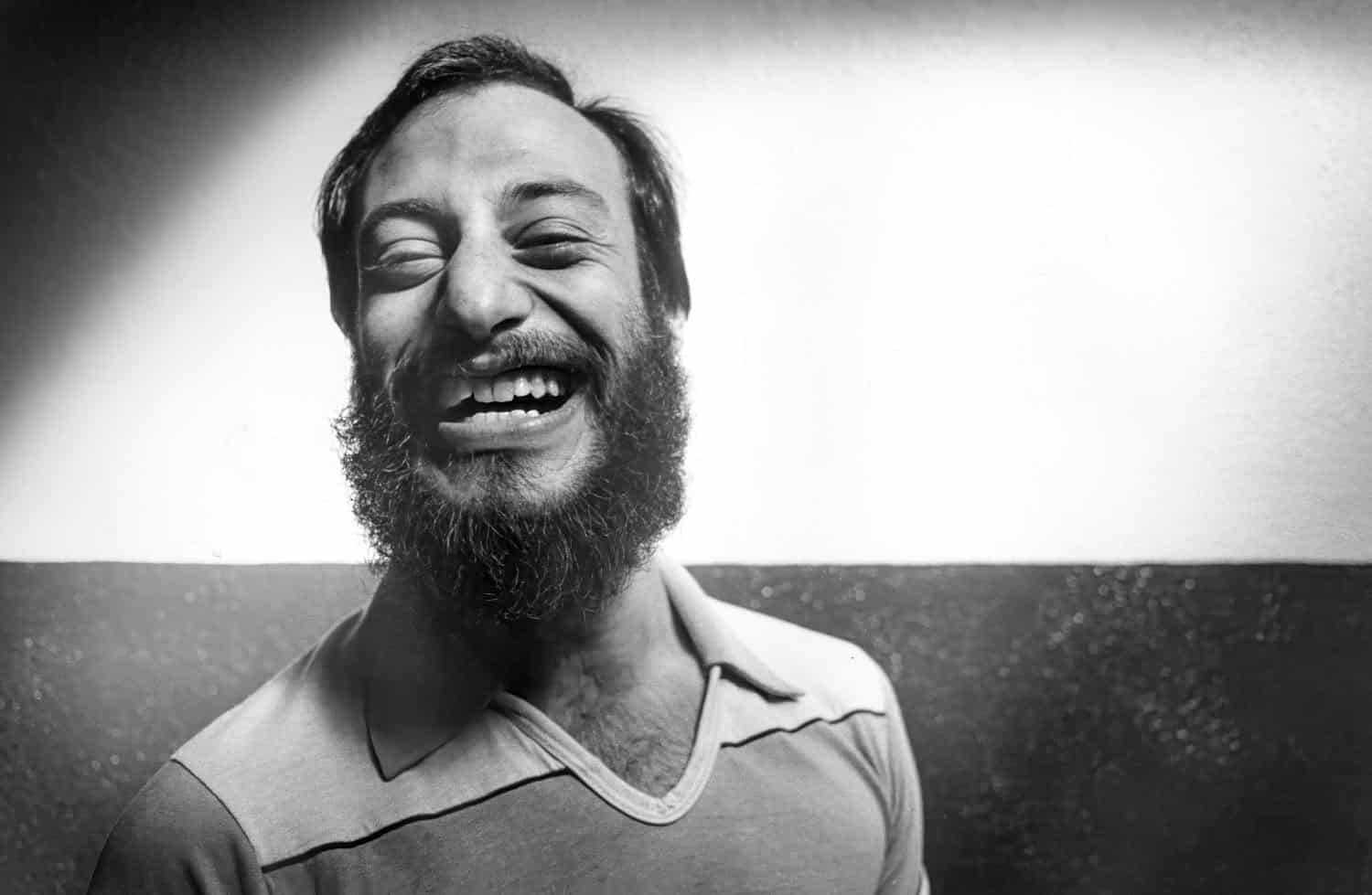 Black-and-white photograph of a middle aged man smiling at the camera. He has a full dark beard and short dark hair. 