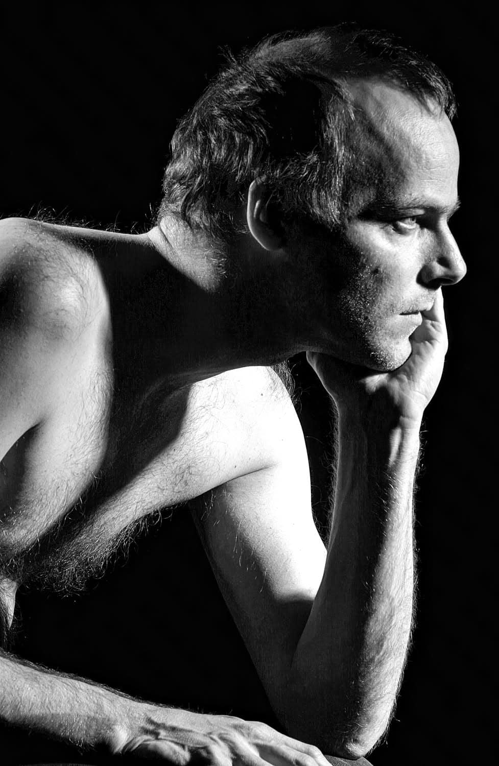 Black-and-white photograph of a shirtless man resting his head on his arm and staring off to the side past the camera.
