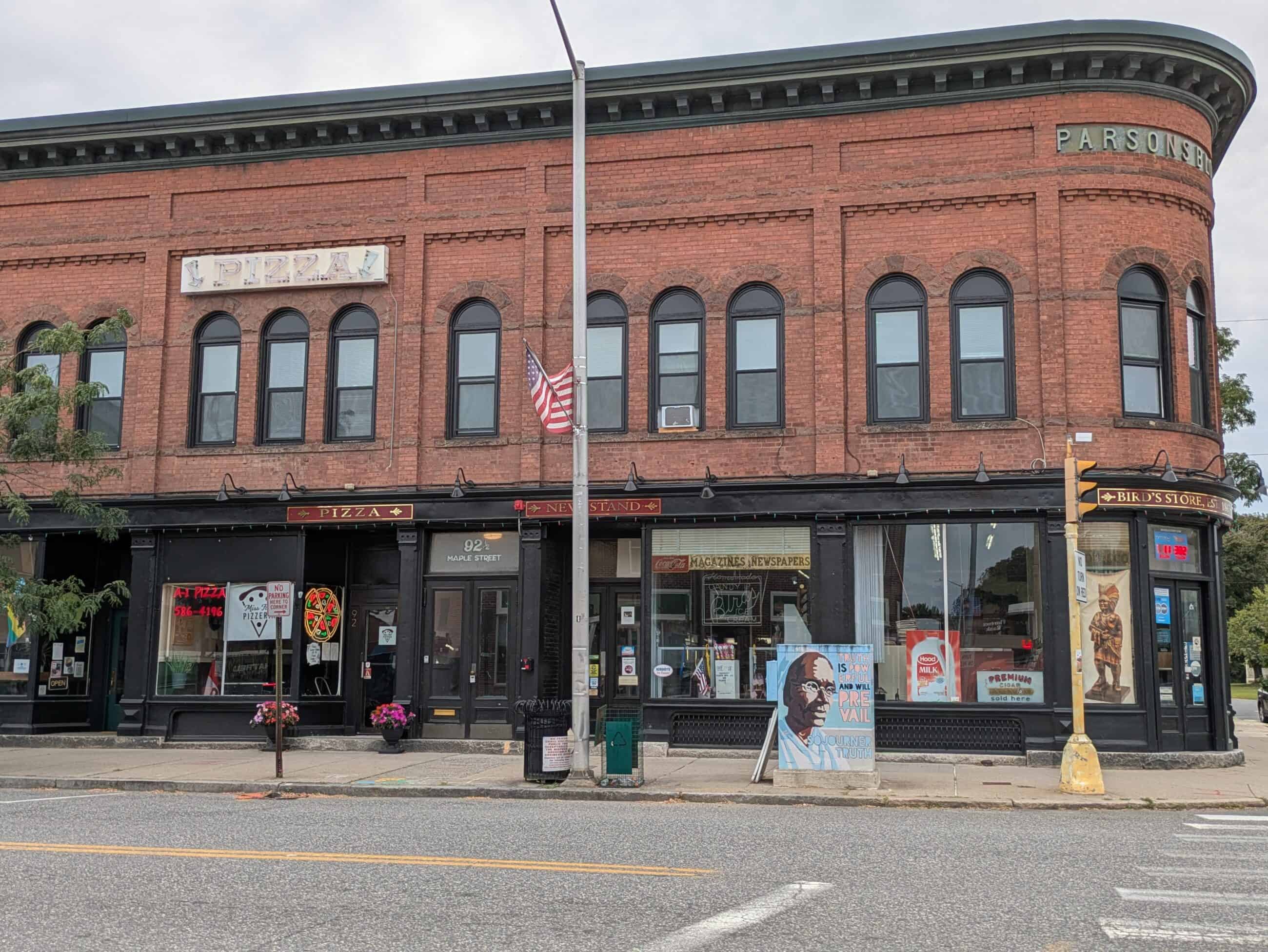 A modern photograph of Parsons Block. Red brick building with black painted first floor storefronts. A large sign is on the top of the building and reads: "PARSONS."