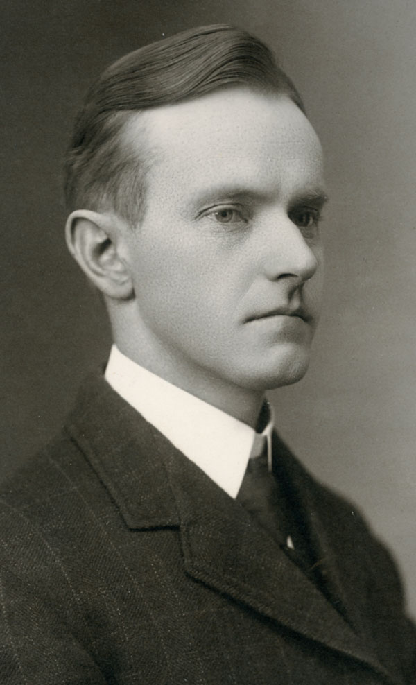 Portrait of a young Calvin Coolidge. He has a black-and-white suit and tie on and a slicked black hairstyle.