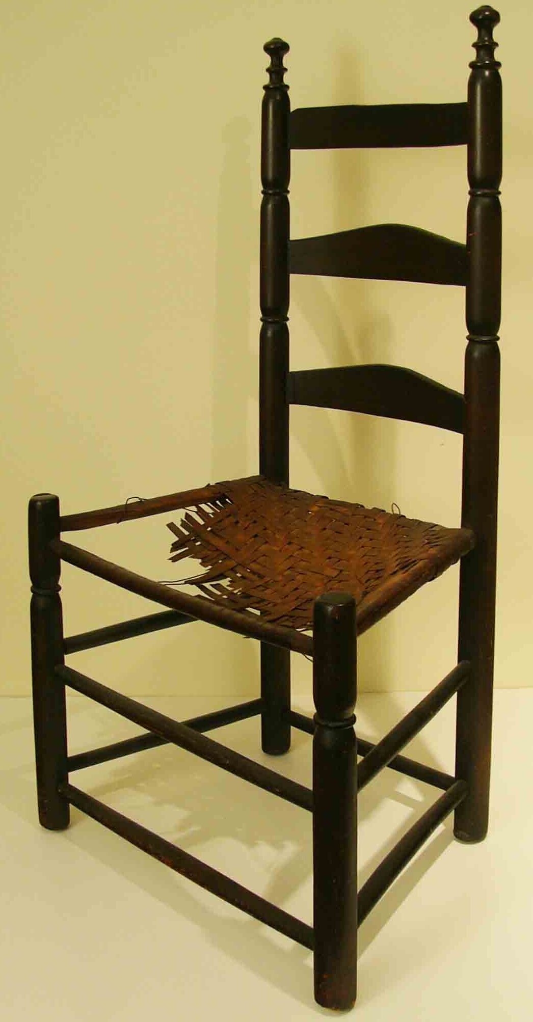 Photograph of a wooden chair with a long back. The seat is damaged.