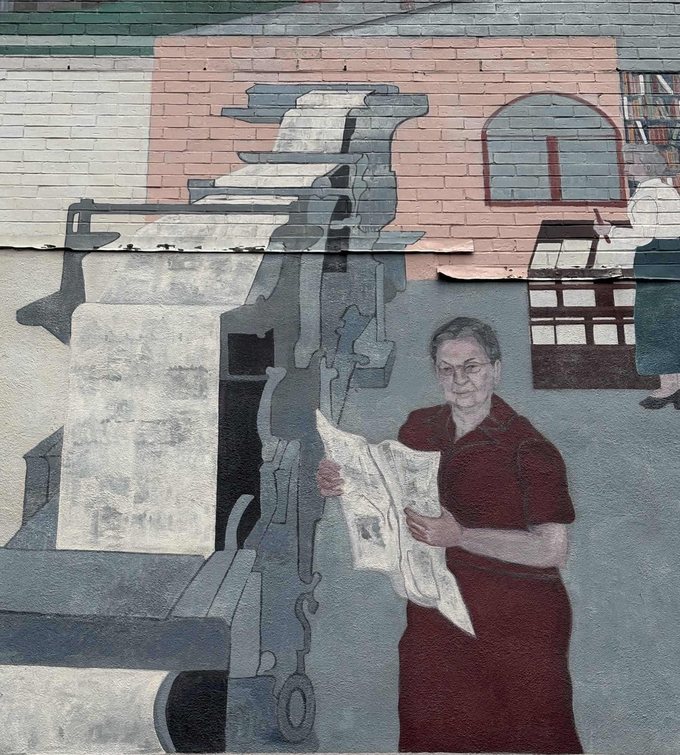 Depiction of a matured Harriet De Rose reading a newspaper next to a newspaper printing machine on the Hestia Mural on Masonic Street. The murial is colorful.