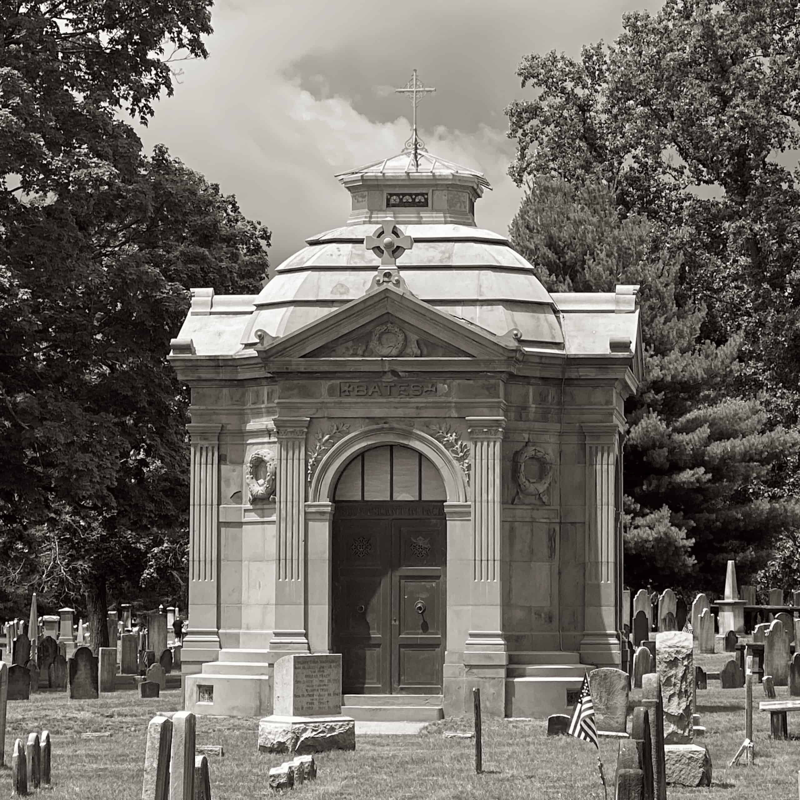 Black & white photograph of a cemetery with a large mausoleum in the foreground with the family name 'Bates' engraved above the doorway.