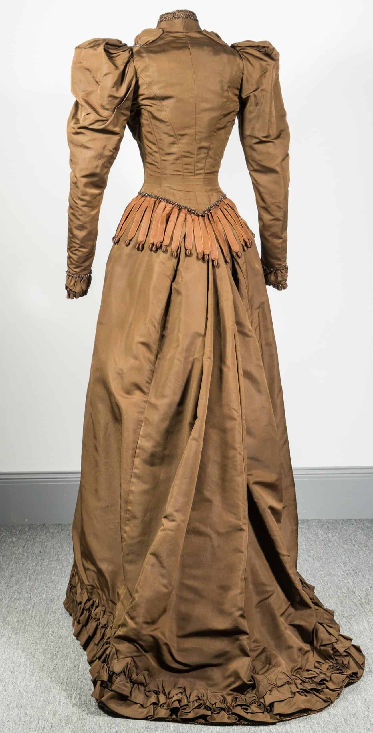 Back of orange-brown wedding dress with a small pointed waist and puffy shoulders.