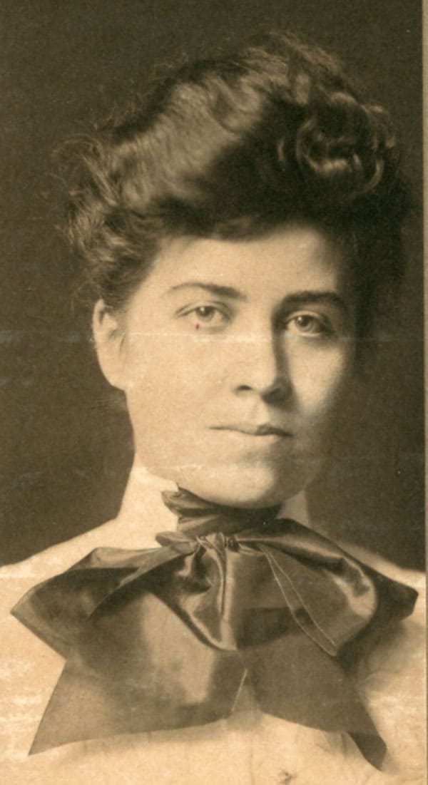 Photographic portrait of Grace Coolidge. She has a rested face, an elaborate updo, and a bow infront of her neck.