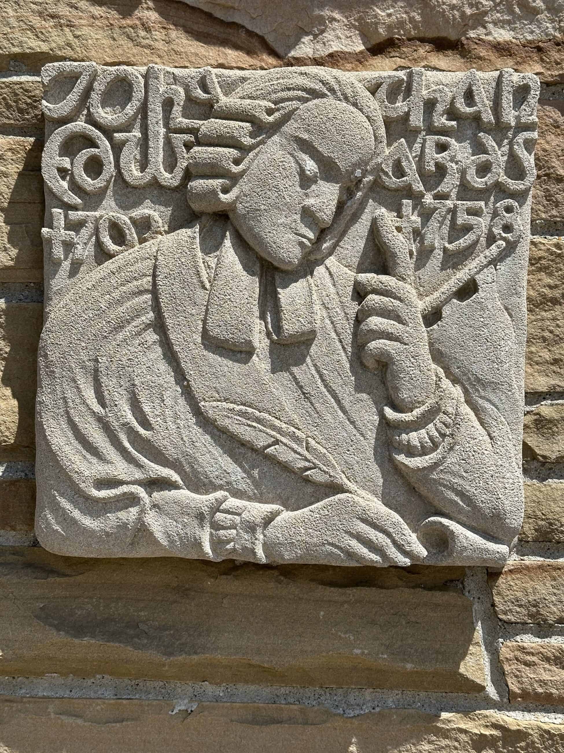 Photograph of the carving of Jonathan Edwards on the wall of Edwards Church. Edwards is drawn in a cartoonish style, and is tilting his head down with his eyes closed in a contemplative manner. His finger is pointing to the sky. 