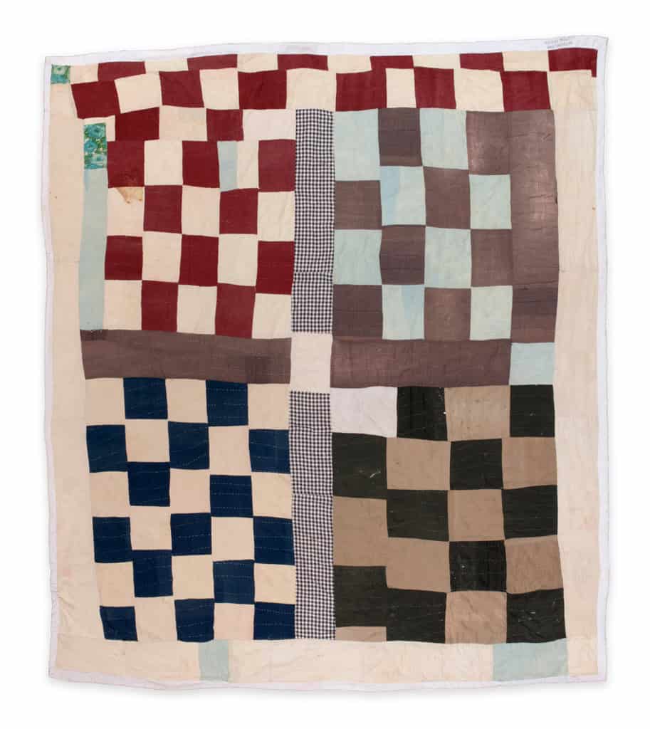 A patchwork quilt featuring a multi-colored four-block checkerboard design separated by sashing strips.