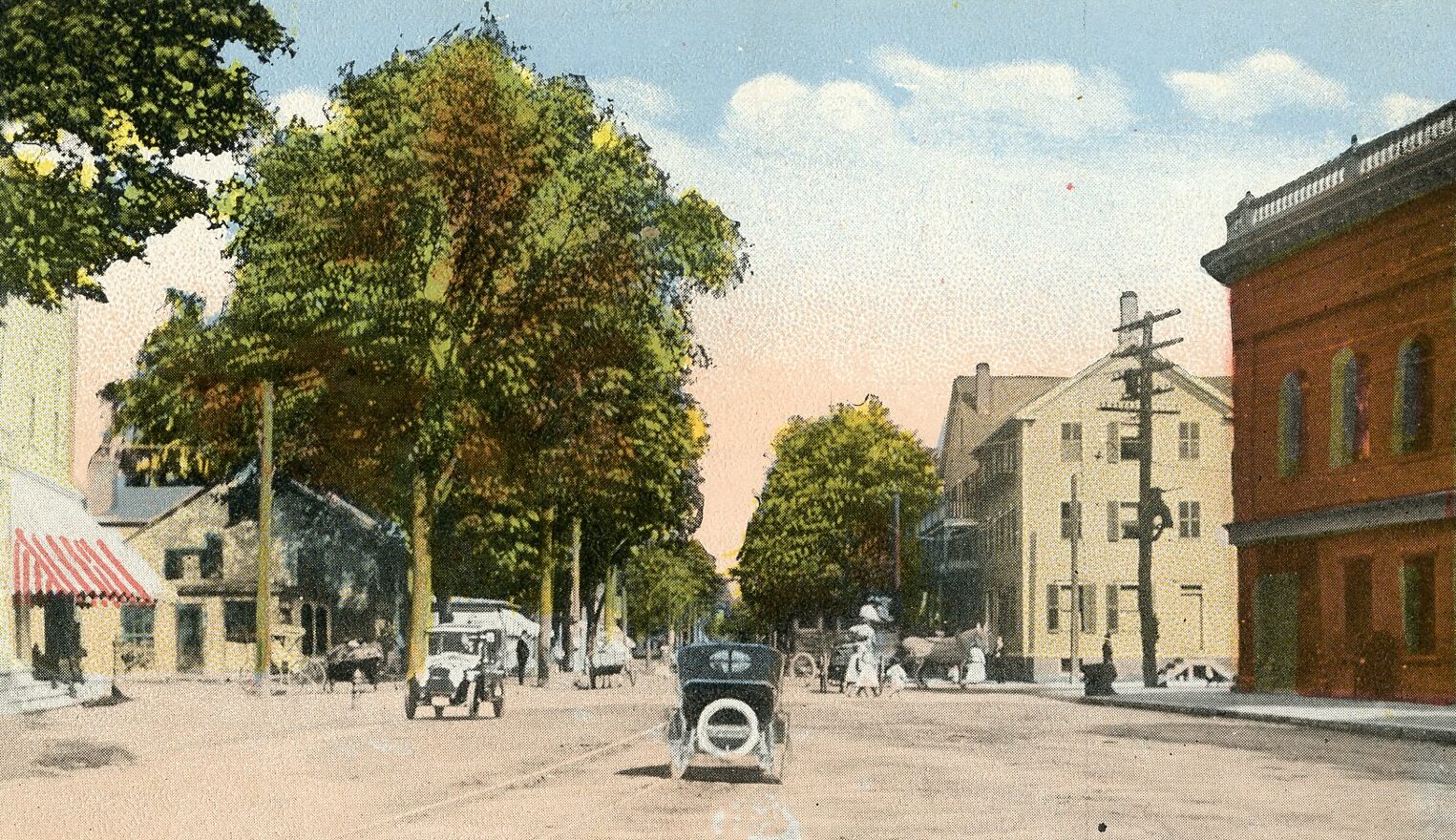Postcard with a photograph that had been colored or a realistic drawing of Downtown Florence. Both cars and horse-drawn carriages are on the road, which is dirt. Trees cover storefronts in the distance.