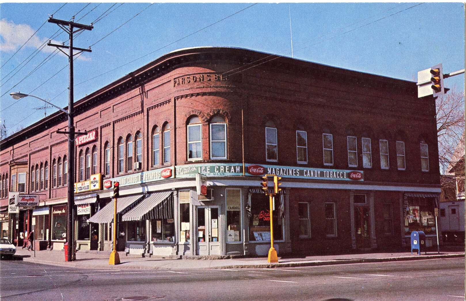 Photograph of Parsons Block. Storefronts in view as well as a bit of the road and light signals. The building is red brick with colorful signs decorating the front.