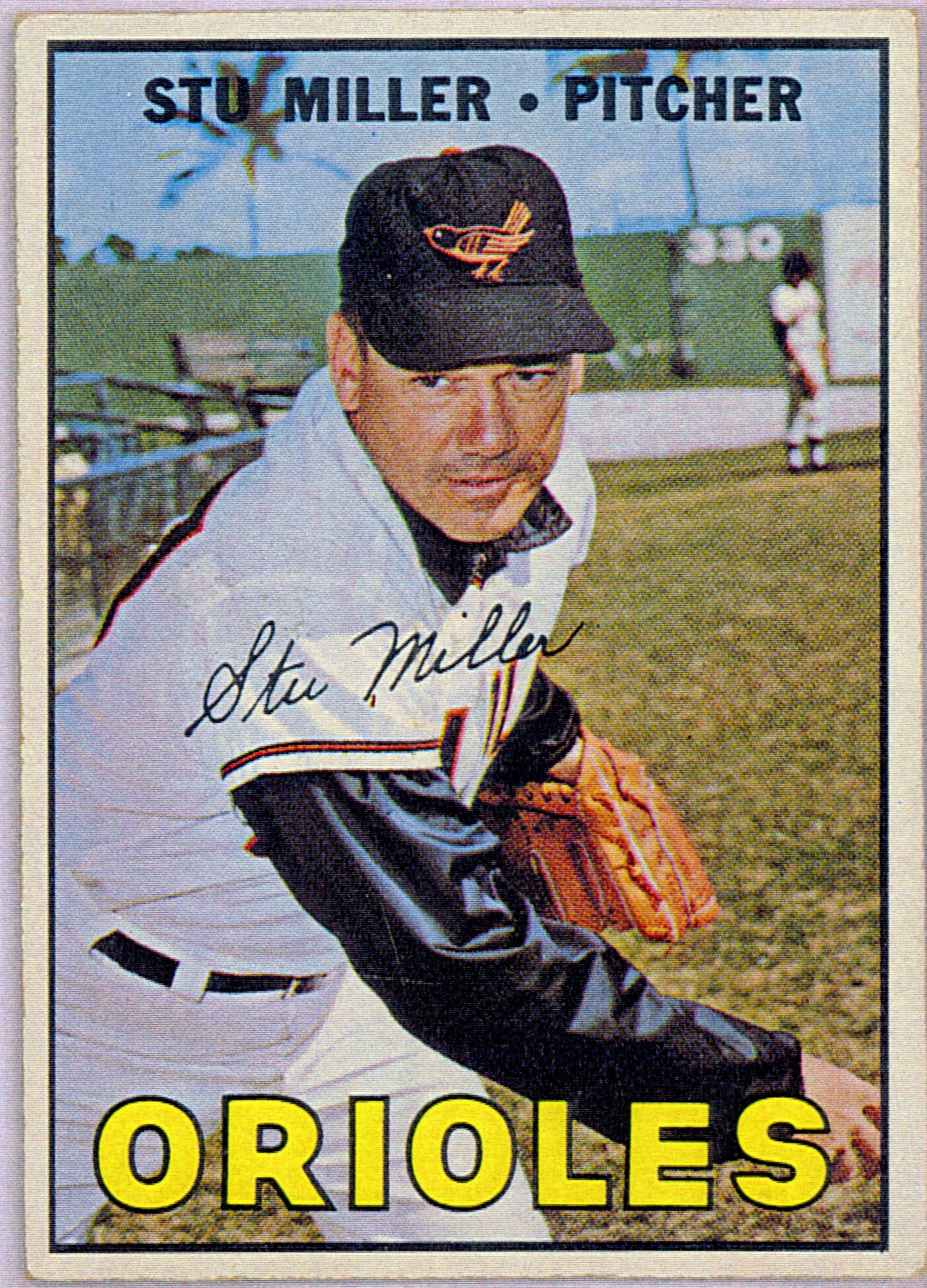 Baseball trading card with a color photograph of a male baseball player in a Baltimore Orioles uniform, with a black ball cap with an orange bird embroidered onto it. He is posed as if he has just thrown a baseball. Text  overlay reads "Stu Miller Pitcher" at the top and "Orioles" in yellow text at the bottom. The card is signed by Stu Miller in the center.