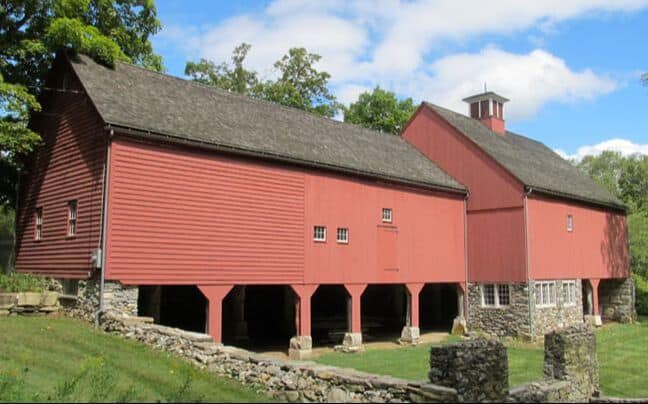 A red wooden barn with a stone base and a small cupola on a green hillside.