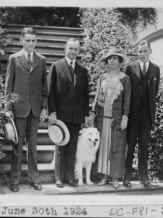 Calvin and Grace Coolidge stand with their sons and dog in formal dress at the foot of an outdoor staircase. The photo has a date June 30th 1924.