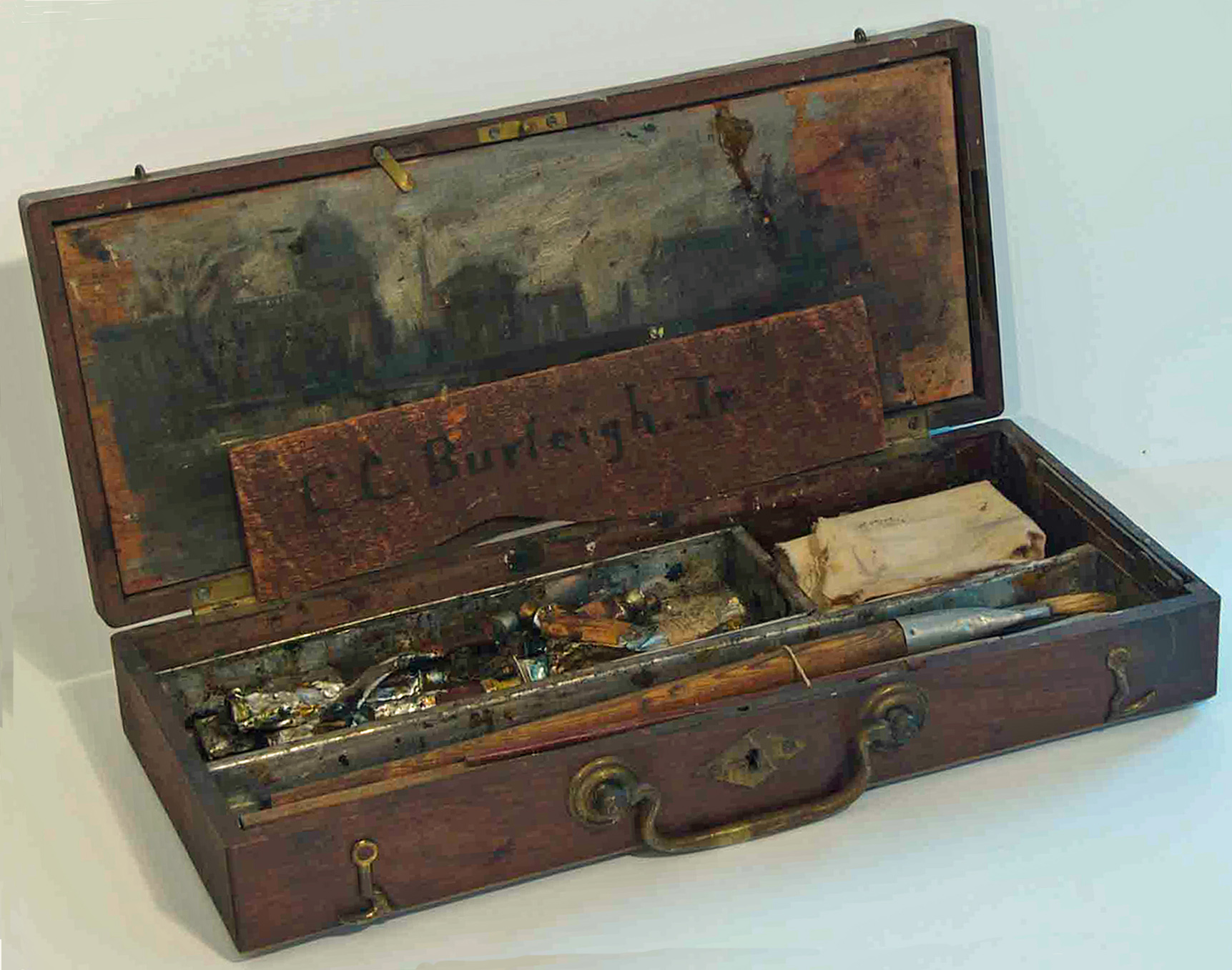A well-used wooden box of paintbrushes and paints with a wood plaque that says Charles Burleigh