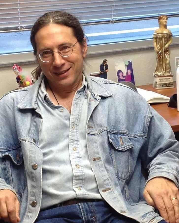 Professor Drew Lopenzina, wearing jean jacket and glasses, smiles at the camera from his office.