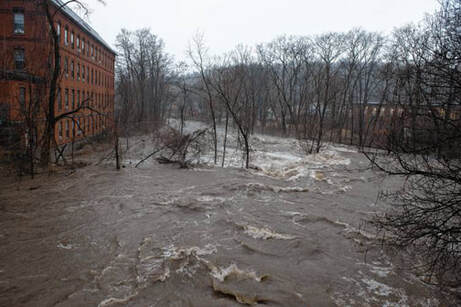 modern photograph of flooding river rushing past a brick building