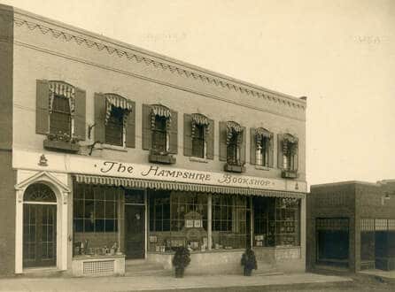 A old sepia-toned photo of a brick building on a hill with the sign: The Hampshire Bookshop. The storefront and second-story windows have striped awnings.