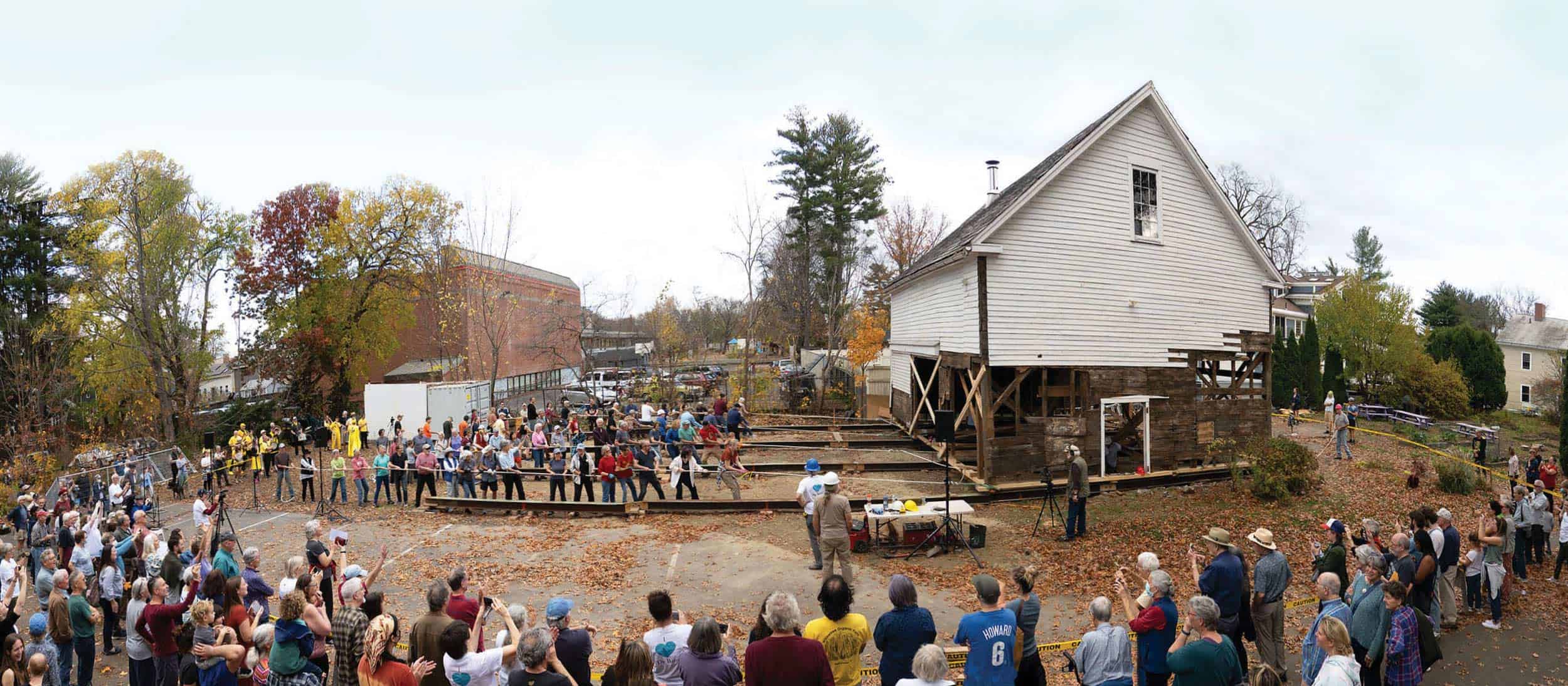 A large group of people all work together to pull a barn into place.