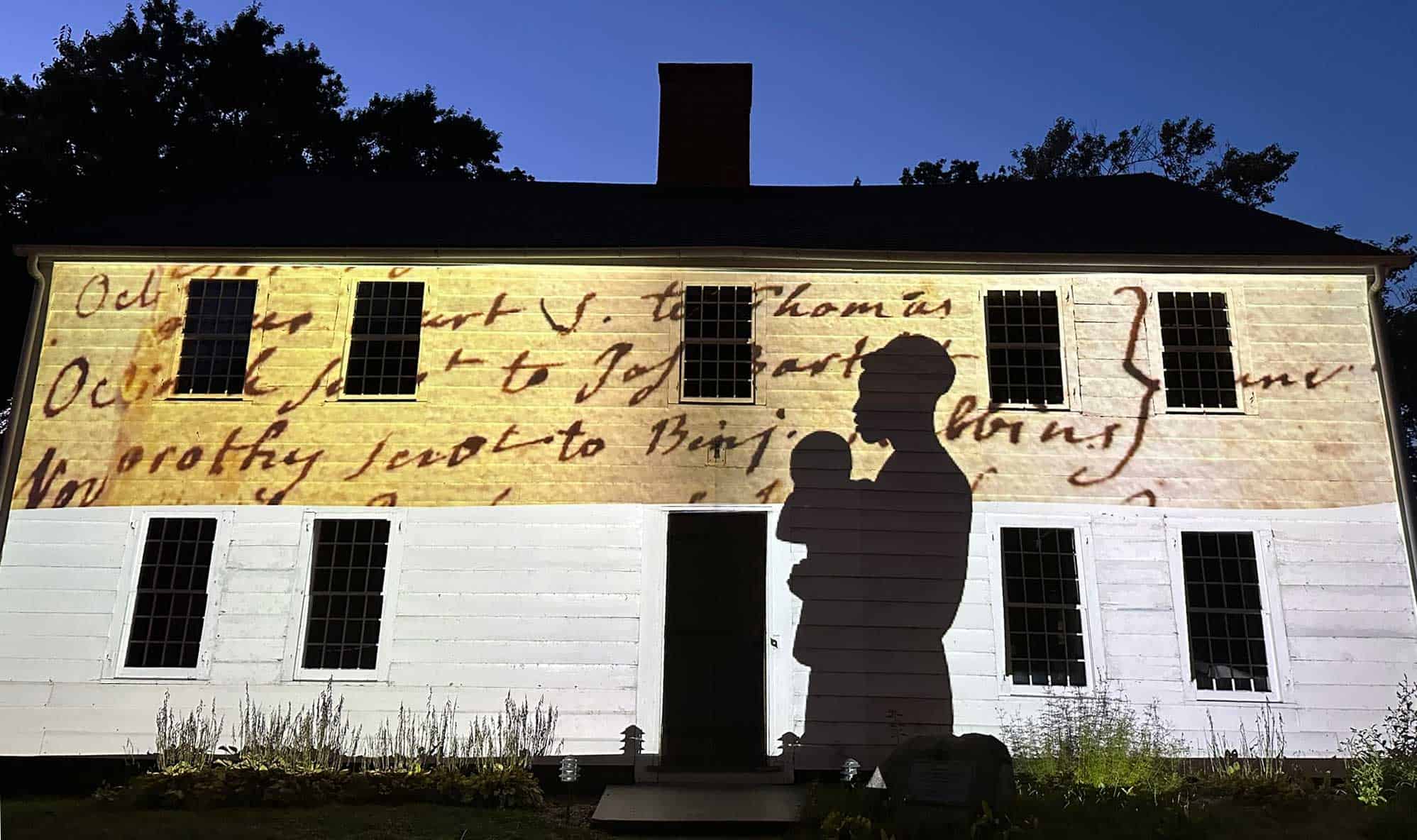 A woman and child's silhouette and a snippet of handwritten script are projected onto the side of a white building.