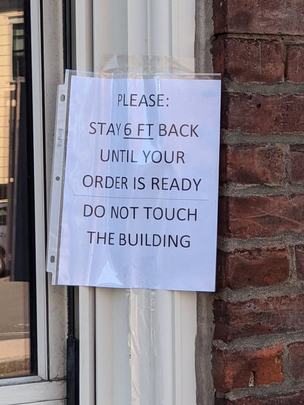 Photo of sign in a window reading "Please Sta 6 ft back until your order is ready. Do not touch the building