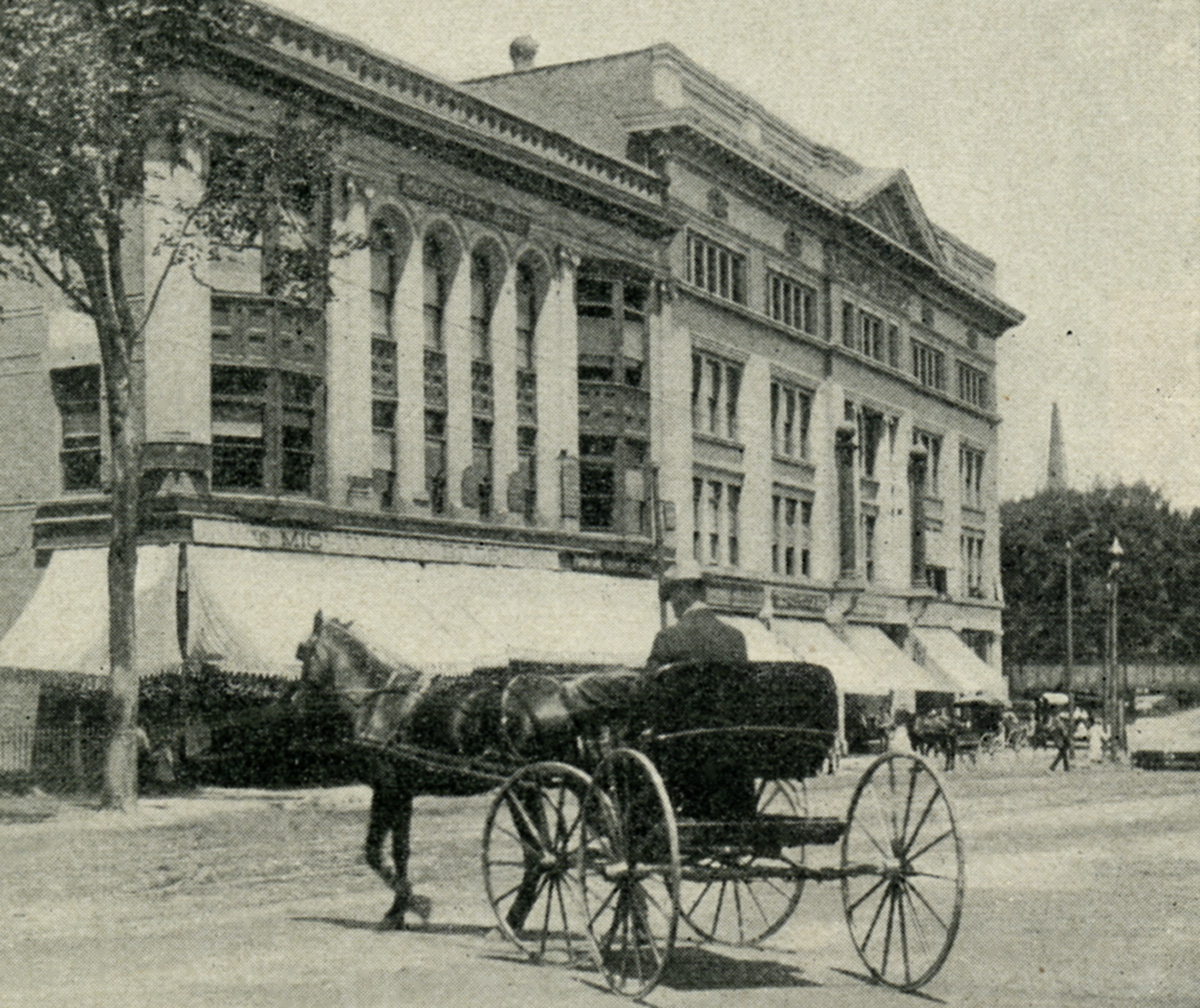 Early 1900s photo of a horse and carriage in front of two imposing brick and stone buildings on a wide street.