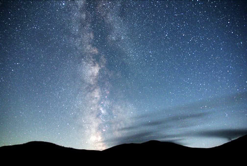 Color photo of stars in the night sky against a sillhouette of the top of a mountan range