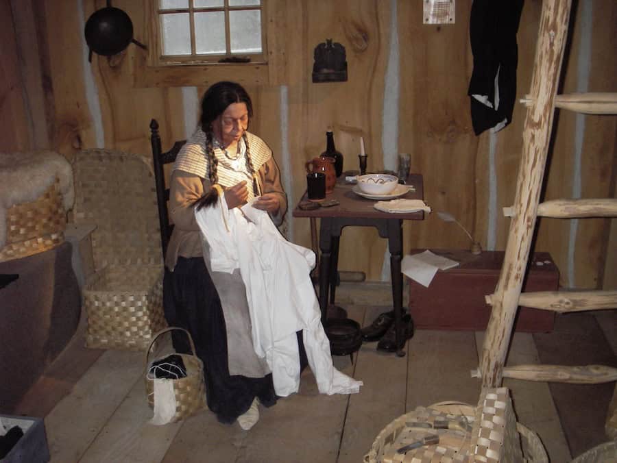 This life-size diorama portrays a Pequot home in the mid-1800s, typifying the ways in which Native people combined Indigenous and European material goods and lifeways. The woman has braided hair, beaded necklace, and deerskin moccasins. Surrounding her are ash-splint baskets used for storage. Diorama at the Mashantucket Pequot Museum. 