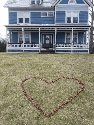 photo of a yard and house. A large heart on the lawn made out of many pine cones