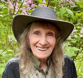 Color photo of a smiling woman in a broad brimmed black hat.