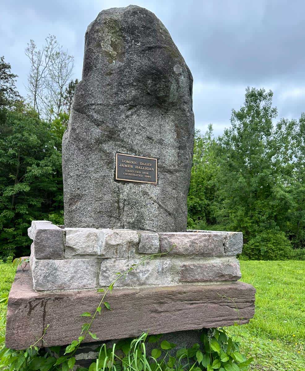 A tall stone with a plaque on a stone foundation.