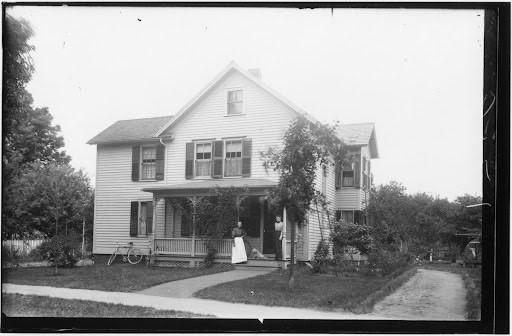 Black-and-white photograph of Sojourner Truth's former home. Two people and a dog stand on the steps of the home. A bike can be seen resting against the front of the building.