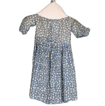 Photograph of a blue and white children's dress. The dress has a lot of yellowing from age, especially on the bodice. The pattern of the dress is blue with a white leaf-like pattern and white vines curling throughout. The waist is high and the sleeves are mid-arm length.