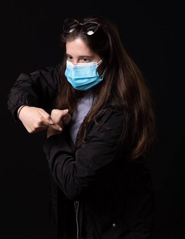 Photo of person wearing face mask and pointing to vaccination spot on upper arm