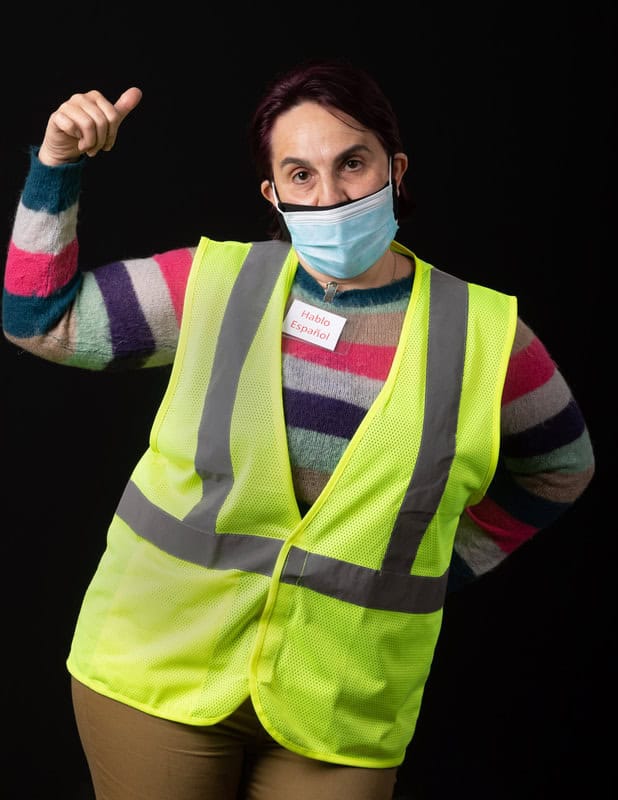 photo of person wearing face mask and a yellow vest with one aheld up