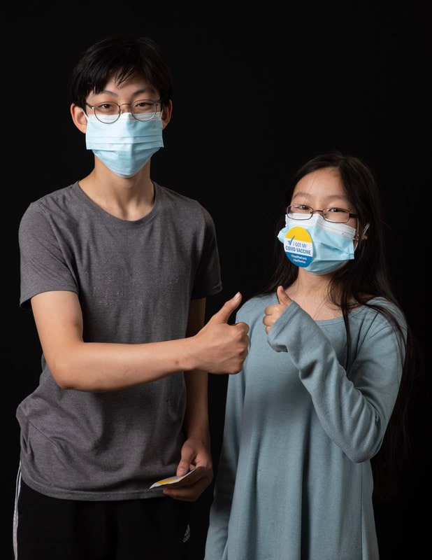 photo of two young people wearing face masks, one with an 'I got my covid vaccine' sticker on their mask