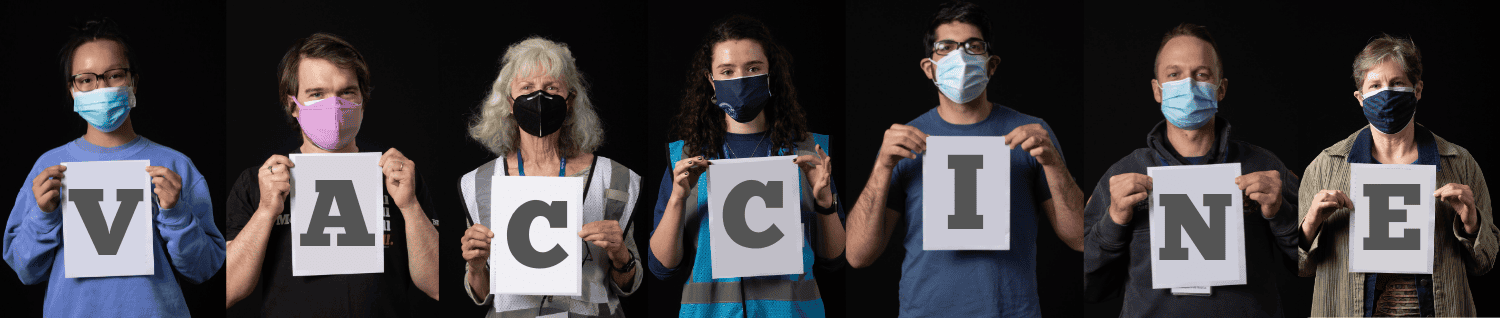 Photograph of seven people each holding up paper with a letter to spell VACCINE